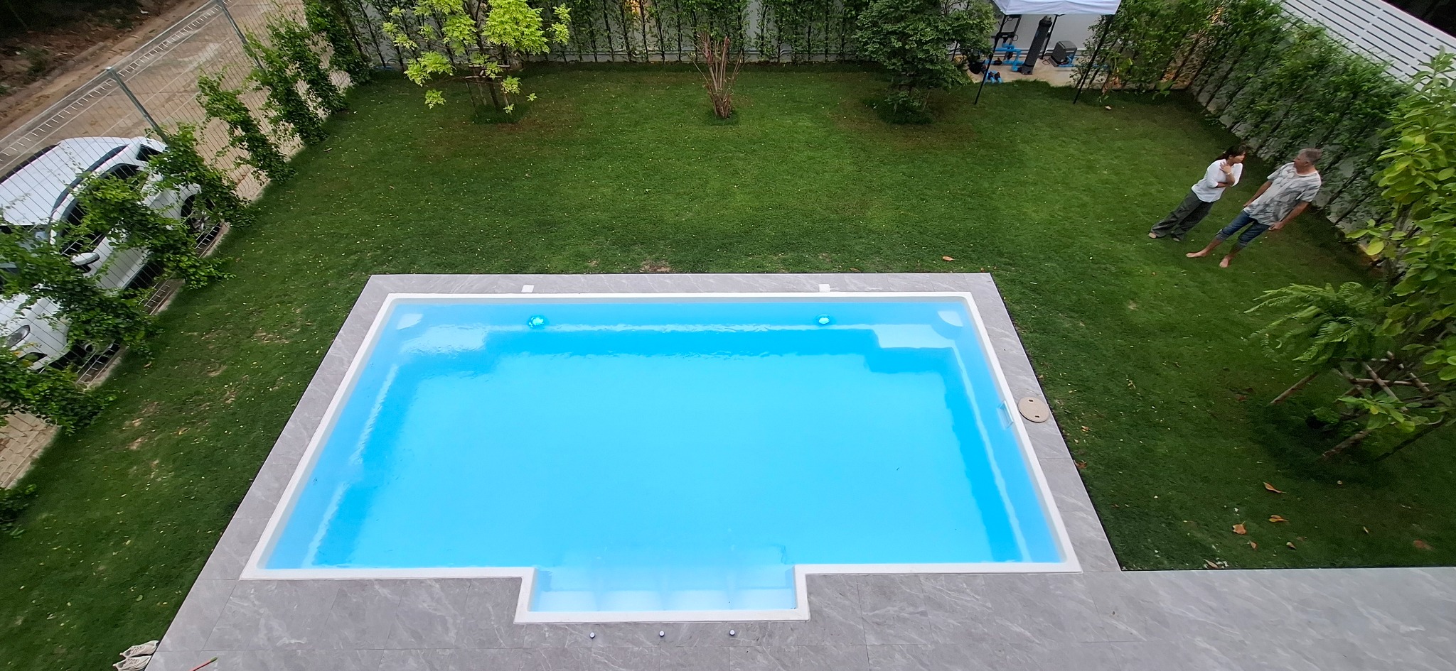 Overhead view of a white swimming pool, tiled surround and garden